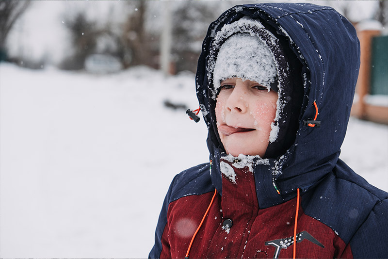 ילד עטוף במעיל מלקק שלג שנופל