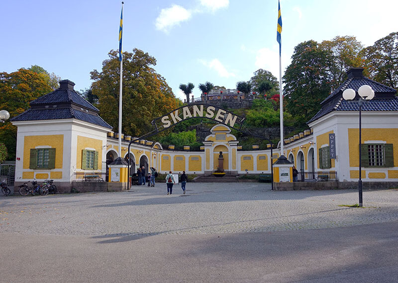 שער הכניסה למוזיאון, בתים לבנים עם גגות שחורים ובאמצע שלט גדול ועליו הכיתוב Skansen
