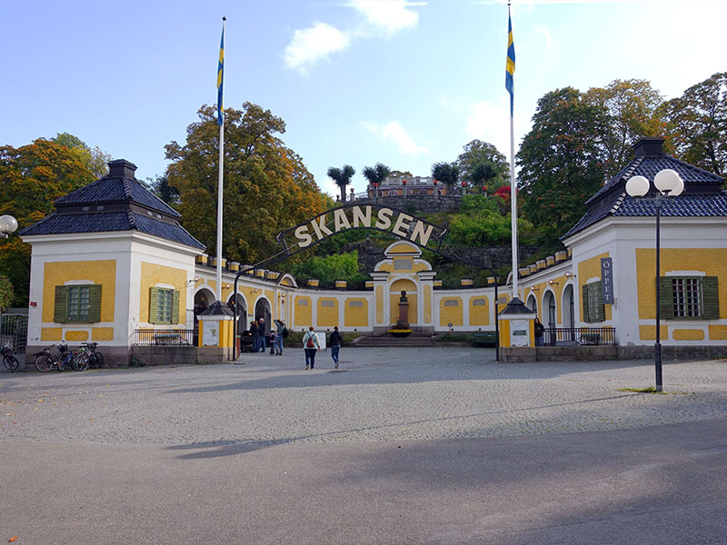 שער הכניסה למוזיאון, בתים לבנים עם גגות שחורים ובאמצע שלט גדול ועליו הכיתוב Skansen