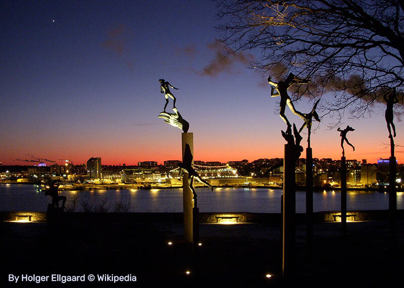 תמונת ערב של גן הפסלים, הפסלים מוארים וברקע העיר שטוקהולם בשקיעה